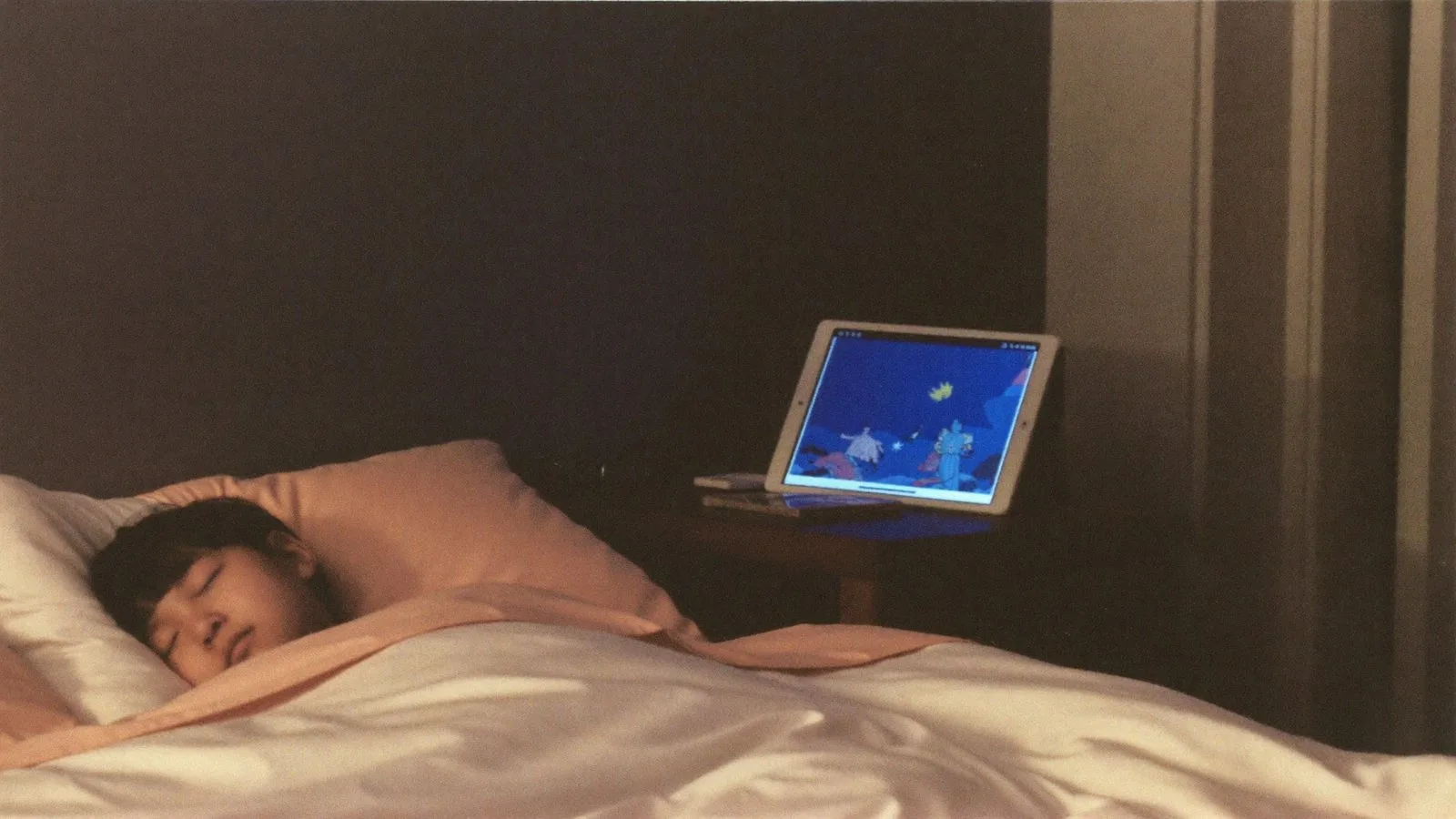 A child asleep in a dim bedroom, a small speaker on the nightstand