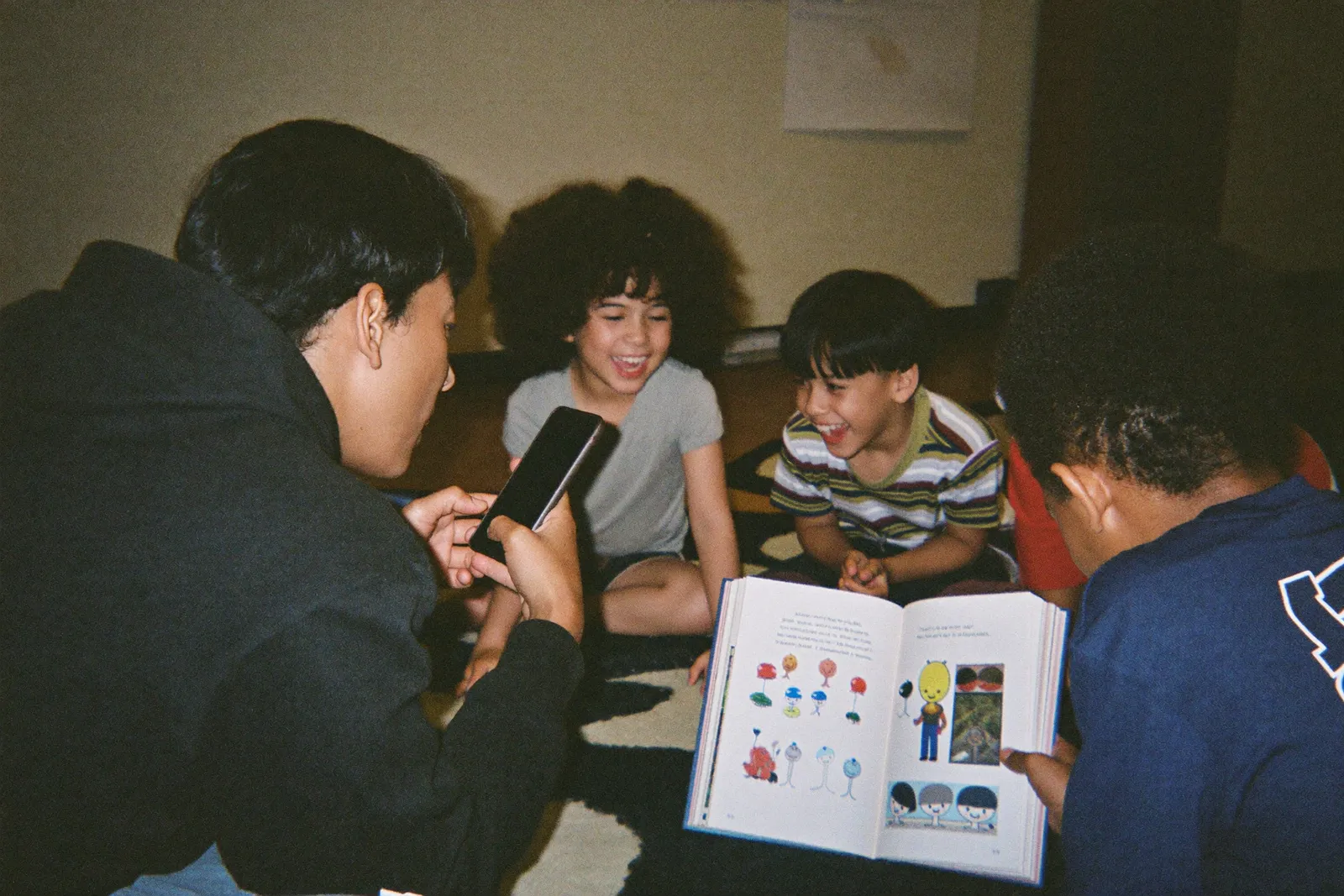 A teacher at her desk in an empty classroom, reading a picture book aloud to her phone